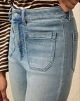 Light blue jeans worn by a person with a striped shirt on a beige background