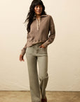 Woman wearing a brown sweater and beige pants against a plain background