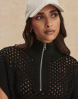 Woman wearing a black sleeveless sweater with a zipper and a beige cap against a beige background