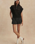 Woman wearing a black sleeveless top and shorts with white sneakers on a beige background