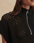 Black knit top with a zipper detail on a neutral background