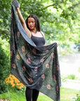 Woman holding a large, patterned shawl in a forest setting