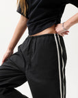 Person wearing black jogger pants with a white stripe on a light background