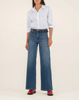 Person wearing a white shirt, blue jeans, and red shoes on a beige background