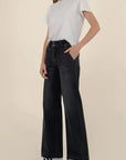 Person wearing black wide-leg jeans and a white t-shirt on a beige background