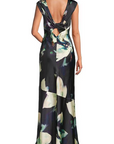 A sleeveless floor-length dress shown from the back on a model, featuring a deep V-neckline with a large bow detail and a dark abstract floral print in black, green, and cream.