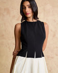 Woman wearing a black top and white skirt against a beige background