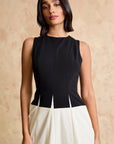 Woman wearing a black sleeveless top and white skirt against a beige background