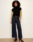 Woman wearing a black turtleneck, yellow long-sleeve shirt, and dark jeans against a white background