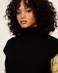 Woman with curly hair wearing a black turtleneck against a white background