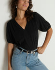 Woman wearing a black top and blue jeans against a plain background