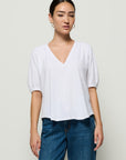 Woman wearing a white blouse and blue jeans against a plain background