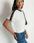 Woman wearing a white t-shirt with black sleeves against a plain background