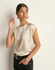 Woman wearing a beige sleeveless top and black pants against a plain background