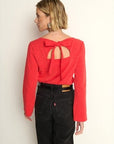 Person wearing a red blouse with a bow detail on the back against a plain background