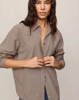 Woman wearing a brown checkered shirt and blue jeans against a plain background