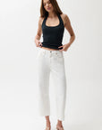 Woman wearing a black tank top and white pants on a white background