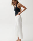 Woman wearing a black halter top and white pants on a white background