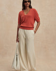 Woman wearing a red sweater and beige pants against a beige background