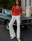 Woman in red sweater and white pants standing in front of a vintage car.