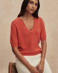 Woman wearing a red sweater and white pants against a beige background