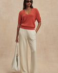 Woman wearing a red sweater and white pants against a beige background