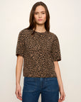 A woman modeling a short-sleeve leopard print top in brown and beige tones, paired with blue jeans, against a plain off-white studio background.