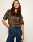 A woman modeling a short-sleeve leopard-print top with dark blue jeans and a black belt, photographed against a plain light background.