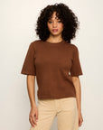 Woman wearing a brown t-shirt and beige pants against a white background