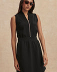 Woman wearing a black sleeveless dress with a zipper on a beige background