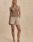 Woman wearing a beige sleeveless top and shorts on a beige background