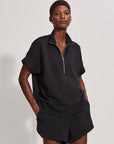 Person wearing a black outfit with a zip-up top and shorts on a white background
