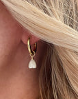 Close-up of a gold hoop earring with a pearl drop worn by a person with blonde hair.