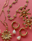 Gold jewelry including necklaces and earrings on a pink background