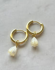 Gold hoop earrings with pearl drops on a marble surface