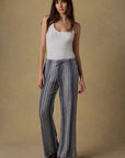 Woman wearing a white tank top and striped pants against a beige background