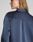 Person wearing a navy blue satin shirt on a plain background