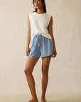 Woman wearing a white sleeveless top and blue checkered shorts on a beige background