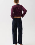A model shown from the back wearing a cropped long-sleeve striped top in dark red and navy, paired with dark navy wide-leg pants and black shoes, against a plain white studio background.
