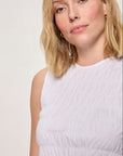 Woman wearing a white sleeveless top against a plain background