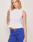 Woman wearing a white sleeveless top and blue pants against a plain background