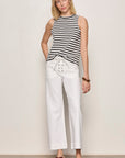 Woman wearing a black and white striped sleeveless top and white pants against a plain background