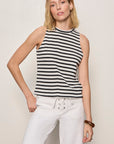 Woman wearing a black and white striped sleeveless top and white pants against a plain background