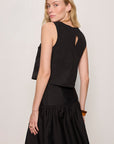 Woman wearing a black sleeveless top and skirt set against a plain background