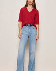 Woman wearing a red shirt and blue jeans against a plain background
