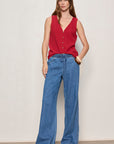 Woman wearing a red sleeveless top and blue jeans against a plain background