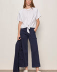 Woman wearing a white top and navy pants against a plain background