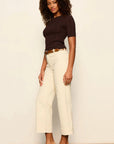 Woman wearing a brown top and white pants against a plain background