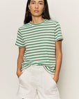 Woman wearing a green and white striped shirt and white shorts on a plain background