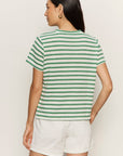Woman wearing a green and white striped shirt and white shorts against a plain background